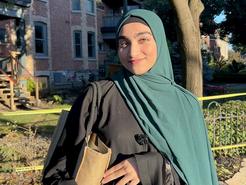 Hafsah Younus standing outside on a sunny day in front of a tree, holding her tote bag.